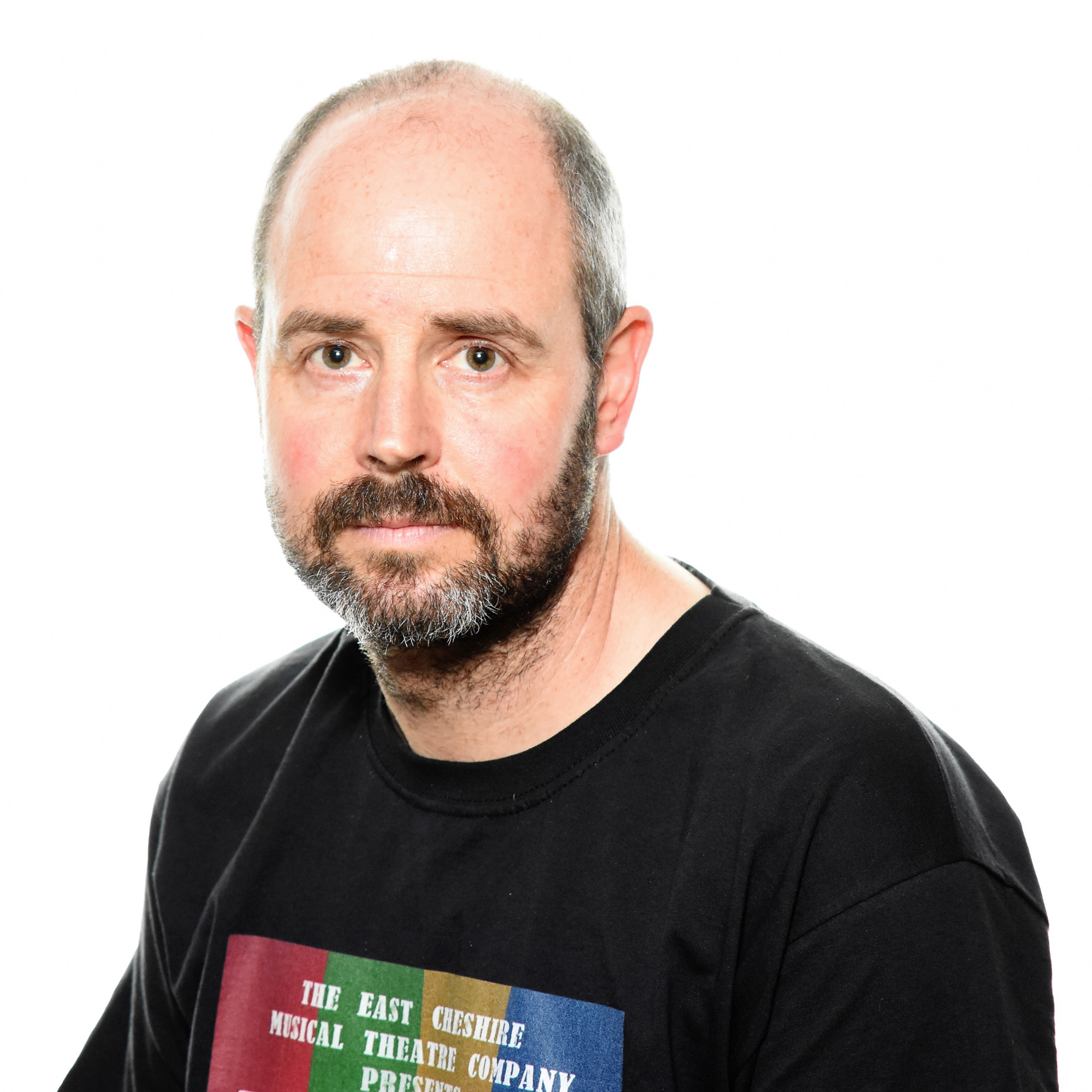 "A professional headshot photography portrait of a middle-aged man with a closely shaved head and a well-groomed beard. He wears a black t-shirt featuring a colorful logo, giving him a relaxed yet confident appearance. The crisp white background and even lighting make this an excellent corporate or artistic headshot."